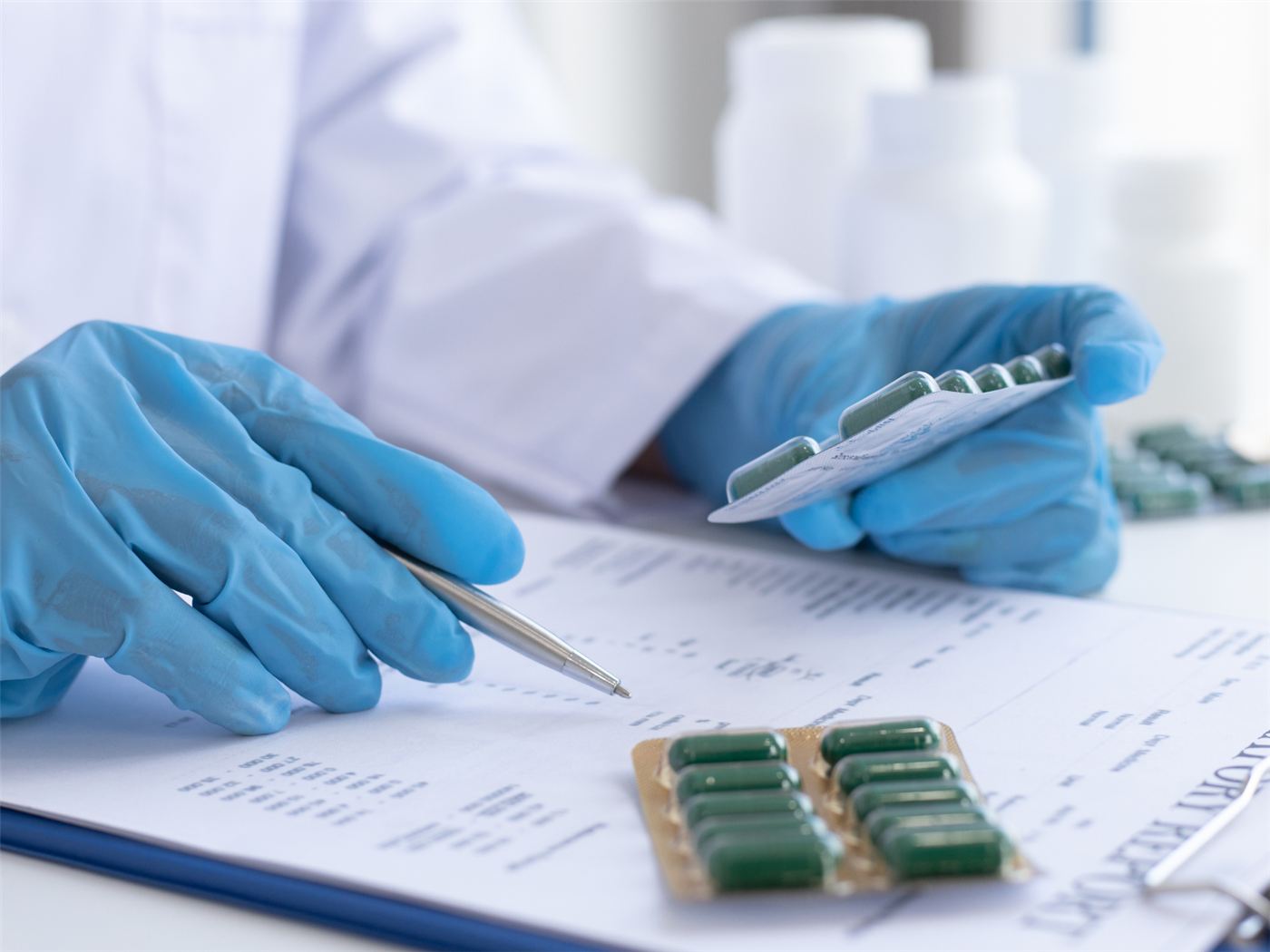 A gloved hand recording pharmaceutical data on a chart